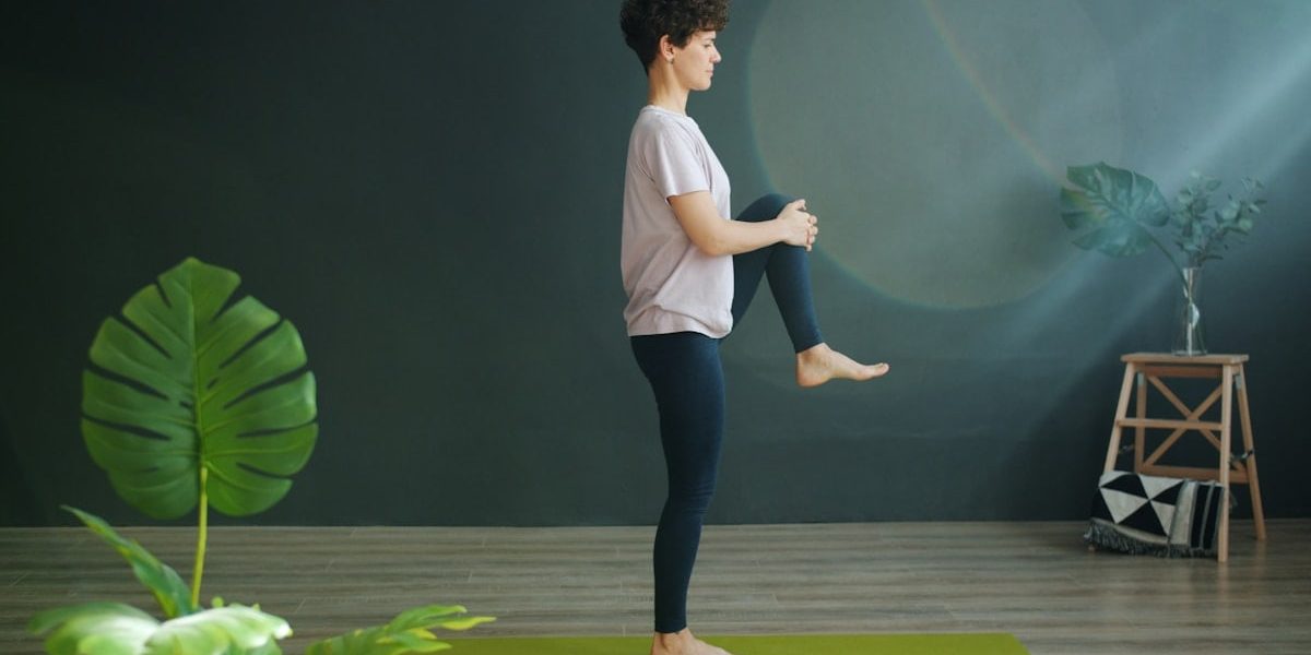 Attractive female adult is doing yoga in wellness studio balancing on one leg relaxing enjoying recreational activity. Modern people, sports and relaxation concept.