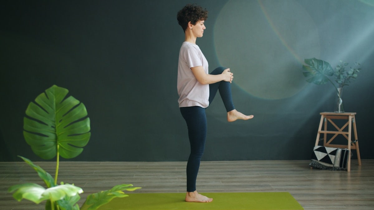Attractive female adult is doing yoga in wellness studio balancing on one leg relaxing enjoying recreational activity. Modern people, sports and relaxation concept.